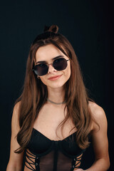 Young beautiful glamour girl posing in semi-transparent black dress and sunglasses on black background