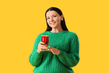 Young woman with glass of mulled wine on yellow background