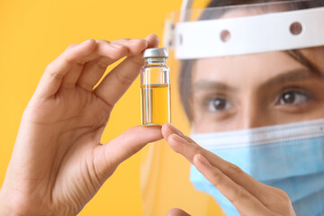 Fototapeta premium Female doctor in protective masks with ampule on yellow background, closeup