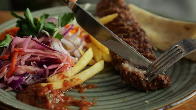Cutting a piece of lula kebab with knife and fork