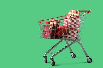 Shopping cart full of Christmas gift boxes on green background