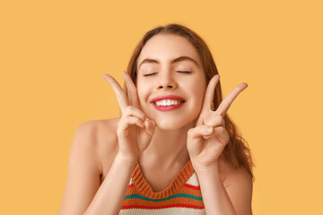 Pretty young woman showing peace gestures on orange background