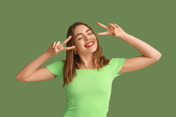 Pretty young woman showing peace gestures on green background