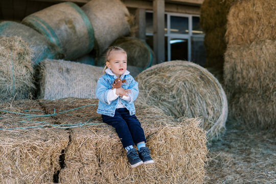 Little girl hugging a soft toy sitting on a haystack at the farm