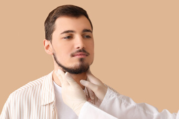 Endocrinologist examining thyroid gland of young man on beige background