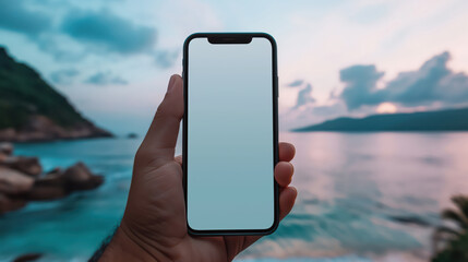 Hand holding smartphone over scenic beach sunset with blank screen
