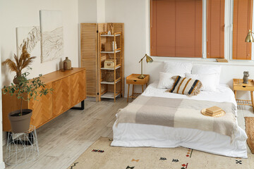 Interior of stylish bedroom with paintings, commode and shelf unit