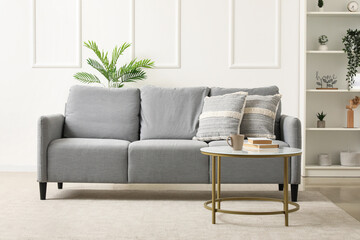 Interior of light living room with grey sofa, table and shelf unit