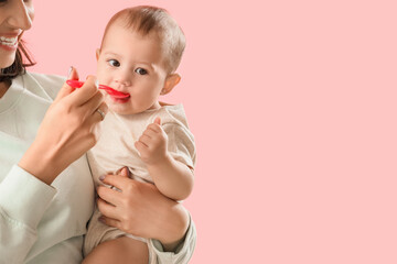 Young woman feeding her little baby with puree on pink background, closeup