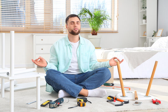 Young man meditating while assembling furniture in bedroom