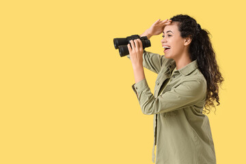 Obraz premium Young African-American woman with binoculars on yellow background