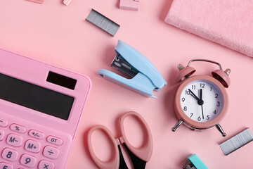 Blue stapler with staples, clips, scissors and alarm clock on pink background