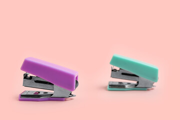 Purple and green staplers on light background