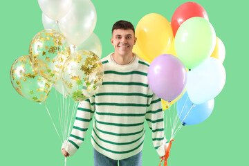 Young man with bunches of colorful balloons on green background