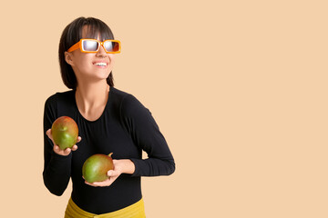 Beautiful young woman with ripe mangoes on beige background