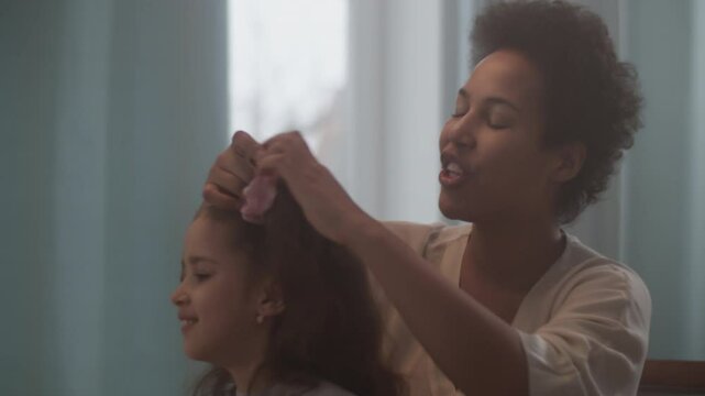 Smiling black woman tying daughter hair with scrunchie
