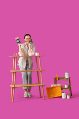 Young woman painting wooden shelf unit on purple background