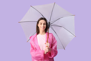 Young woman in raincoat with opened umbrella on lilac background