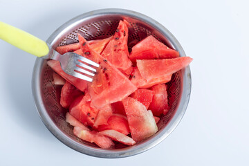 Freshly cut watermelon slices in a stainless steel colander with fork