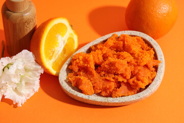 Plate with natural body scrub, flower and oranges on color background