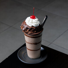 Chocolate milkshake topped with a brownie, whipped cream and a cherry, ready to be enjoyed