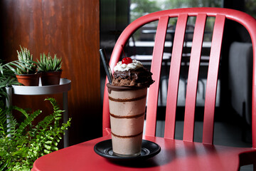 Indulgent mocha frappe topped with chocolate and a cherry, served in a stylish glass on a red chair in a cafeteria setting