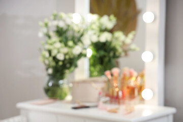 Blurred view of decorative cosmetics and vase with flowers on table in dressing room