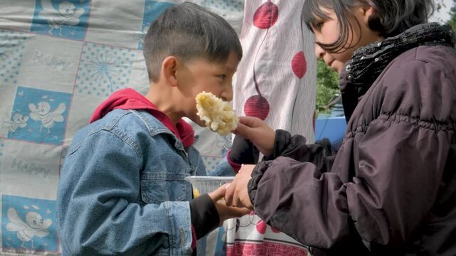 slow motion latin boy eating a choclo con queso with his sister in the streets of the city of la paz, bolivia - street gastronomy concept