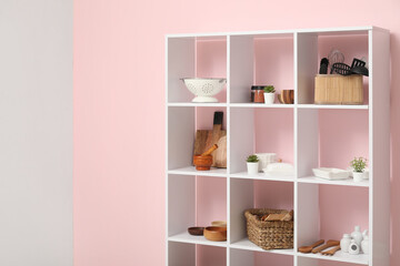 Modern shelving unit with kitchen utensils near pink wall in kitchen