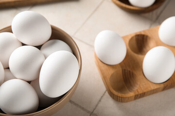 Bowl and wooden holder with raw chicken eggs on white tile background