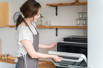 キッチンでキッチンで電子レンジを使う女性（笑顔）  © buritora