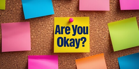 Sticky note with bold black text reading "ARE YOU OKAY?" pinned to a corkboard among colorful handwritten notes, symbolizing mental health awareness, empathy, and emotional support.

