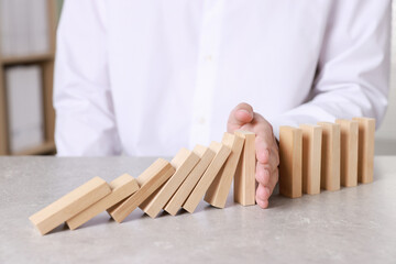 Man stopping wooden blocks from falling at table, closeup. Domino effect