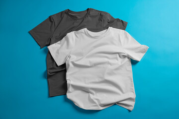 Blank t-shirts on light blue background, flat lay. Mockup for design