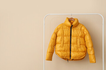Rack with yellow puffer jacket near beige wall