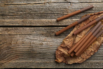 Dried tobacco leaf and cigarettes on wooden table, top view. Space for text