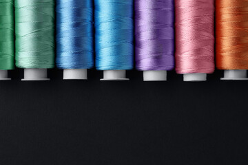 Spools of colorful sewing threads on black background, flat lay. Space for text