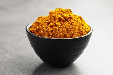 Turmeric powder in bowl on grey table, closeup