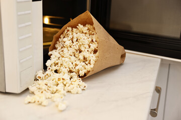 Tasty popcorn in paper bag near microwave oven on white marble countertop indoors, closeup