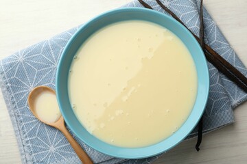 Tasty condensed milk, spoon and vanilla pods on white wooden table, flat lay