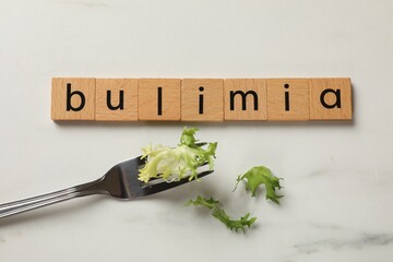 Word Bulimia and fork with lettuce on white marble table, top view