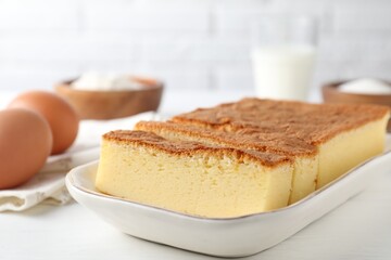 Tasty Japanese Castella sponge cake and ingredients on white table, closeup