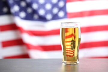 Glass of beer on table against flag of USA, space for text