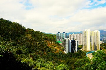 Panorama na miasto Hongkong, wysokie wieżowce i górę w ich otoczeniu. Budynki Hongkongu, droga i bliskość natury. Widok na Hongkong i liczne zabudowania.