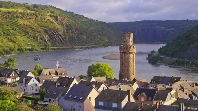 Morning sunrise over the Rhine River Valley with a small riverside town, Oberwesel, a Medieval Tower, Ochsenturm, and romantic rolling hills with vineyards, Germany