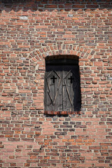 Close-up of the facade of an old building with brickwork, an arched window with wooden shutters decorated with crosses. The texture of the brick, the play of light and shadow, of historical charm