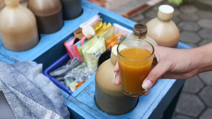 A traditional herbal medicine or known in Indonesia as 'jamu kunyit asem' seller is giving a glass of herbal medicine to the buyer