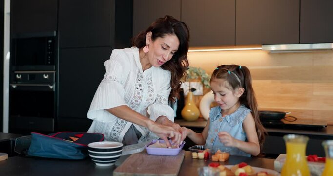 Happy mother, child and morning with bag for school, breakfast or getting ready together in kitchen at home. Mom, daughter and kid with lunch box for meal prep, food or kindergarten snack at house