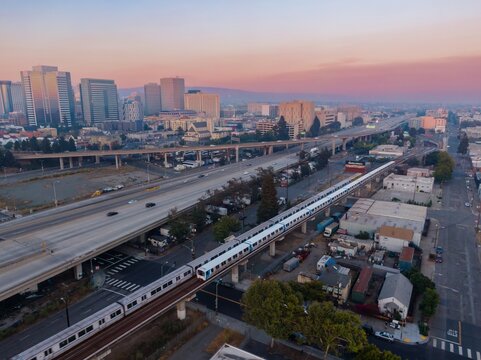 Aerial view of a BART train traveling through Oakland, California, USA, at sunset. Commuters use public transit to travel to and from the city.