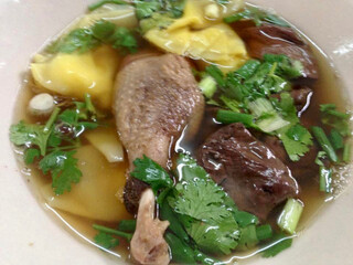 Clear broth, Dumplings with duck leg and blood, A bowl of duck wonton soup is beautifully presented, with tender duck slices and delicate wontons floating in a clear, savory broth.